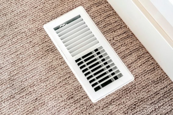 White air conditioner duct grille cover against floor with brown carpet