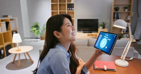 asian young woman using smart home app to control light turning on with tablet pc